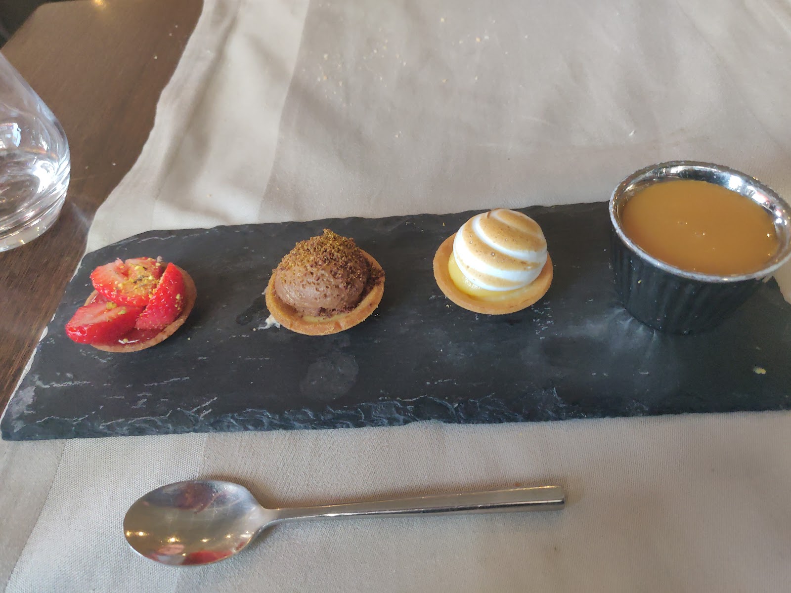 Café gourmand : mini-tartelettes fraise, mousse chocolat, citron meringué et crème caramel sur une ardoise