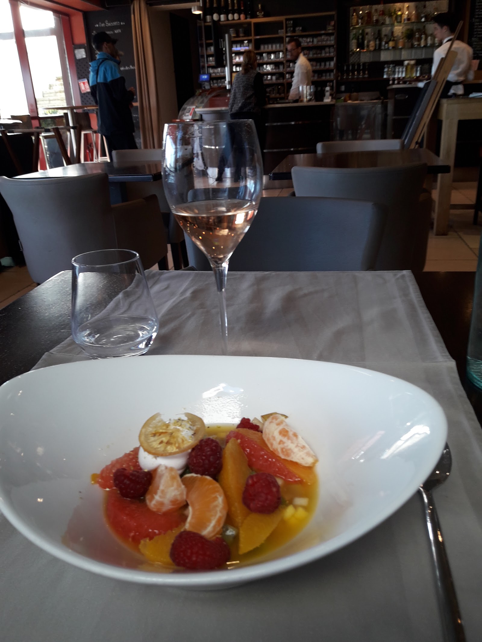 Un verre de rosé devant la salle et le bar du Forum, dessert d'agrumes et framboises au premier plan